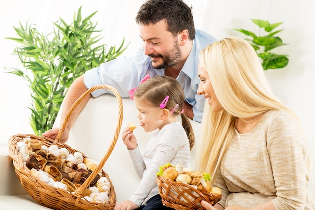 Foto familia feliz juntos, padres con hija sentada en el sofá de la sala de estar frente a cestas tejidas llenas de productos horneados, eligiendo el próximo refrigerio.