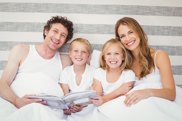 Familia feliz leyendo un libro sobre la cama