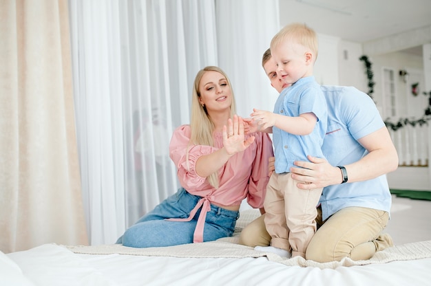 Familia feliz con un lindo bebé. Mamá, papá e hijo juegan en la cama en una habitación luminosa y acogedora en casa.