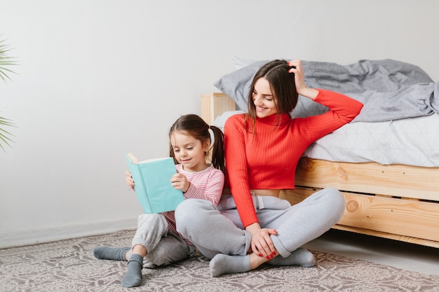 Familia feliz madre e hija hija leyendo sosteniendo el libro acostado en la cama