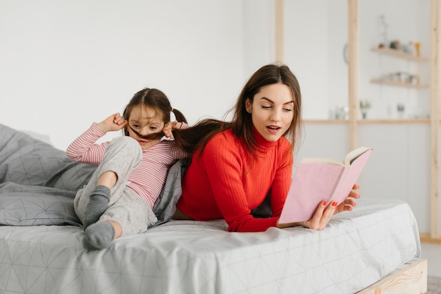 Familia feliz madre e hija hija leyendo sosteniendo el libro acostado en la cama