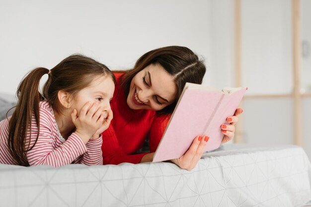 Familia feliz madre e hija hija leyendo sosteniendo el libro acostado en la cama