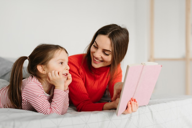 Familia feliz madre e hija hija leyendo sosteniendo el libro acostado en la cama