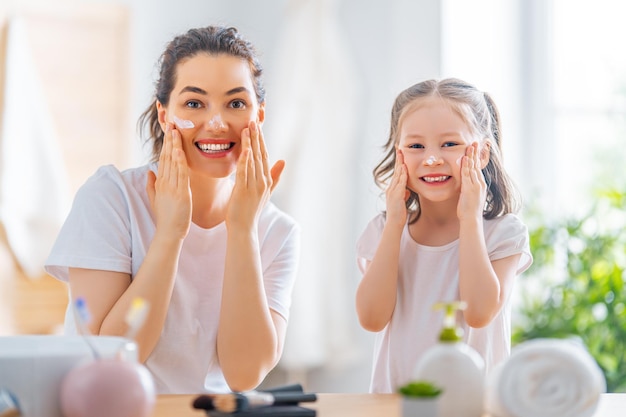 Familia feliz Madre e hija niña están cuidando la piel en el baño