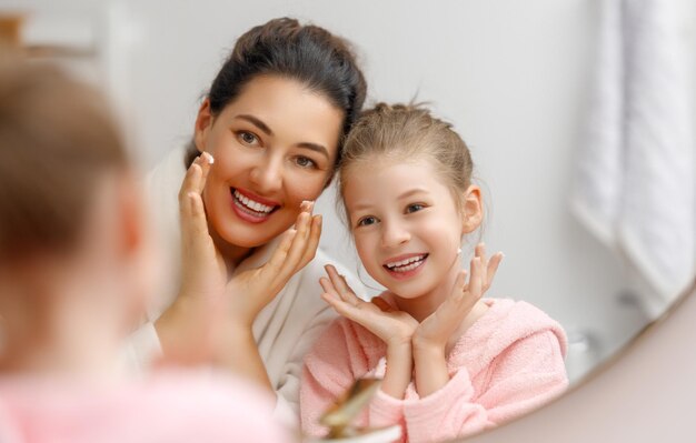 Familia feliz Madre e hija niña están cuidando la piel en el baño