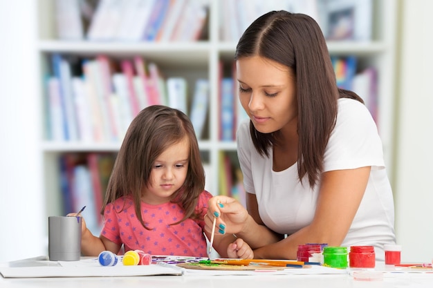 Familia feliz madre e hija pintan juntas. La mujer ayuda a la niña.