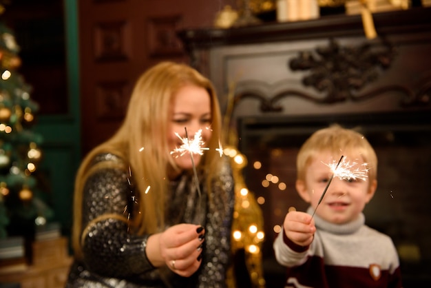 Familia feliz madre e hijo con bengala cerca de un árbol de Navidad.