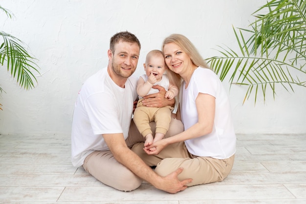 Familia feliz madre padre y bebé abrazan y sonríen a los padres jóvenes en casa