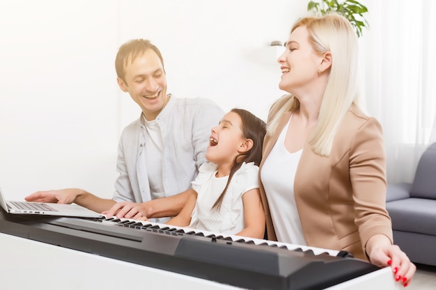 Familia feliz, madre, padre e hija tocando el piano en casa, concepto de relación familiar. escuela de música y música familiar.