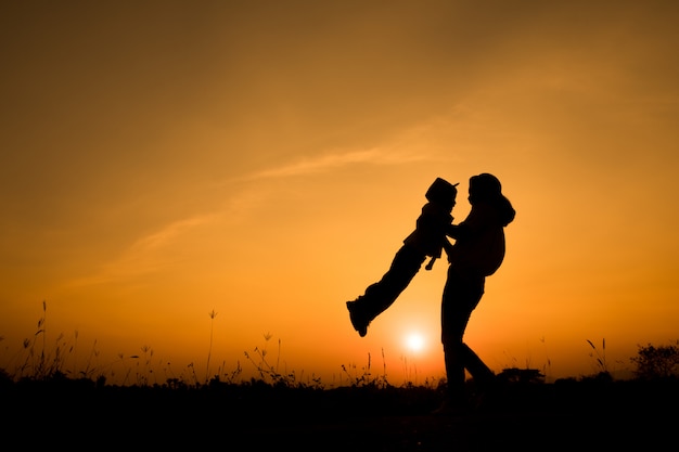 familia feliz. Una madre y su hijo jugando en los campos de hierba al aire libre en la noche silueta