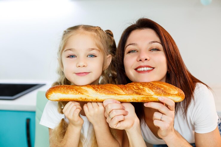 Família feliz, mãe e filha comem um pão mordendo de lados diferentes. Relações familiares da criança com os pais