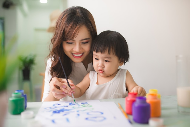 Família feliz mãe e filha pintam juntos. Mulher asiática ajuda a filha dela.