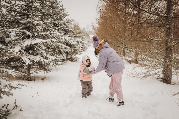 Família feliz mãe e filha se divertem jogando no inverno caminhar ao ar livre. família na floresta de inverno