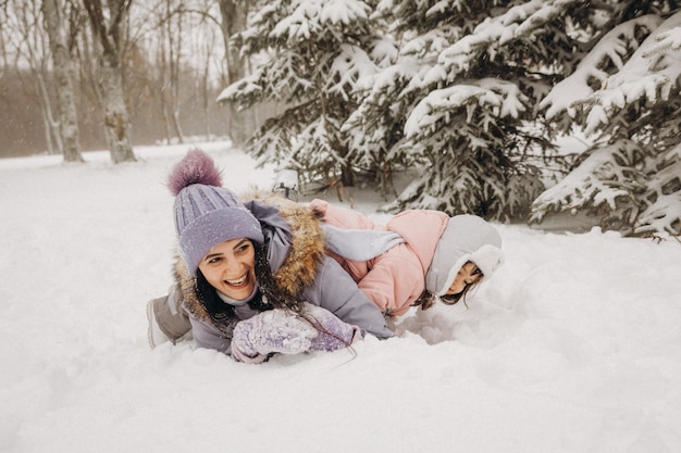 Família feliz mãe e filha se divertem jogando no inverno caminhar ao ar livre. mãe e filho estão deitados na neve.