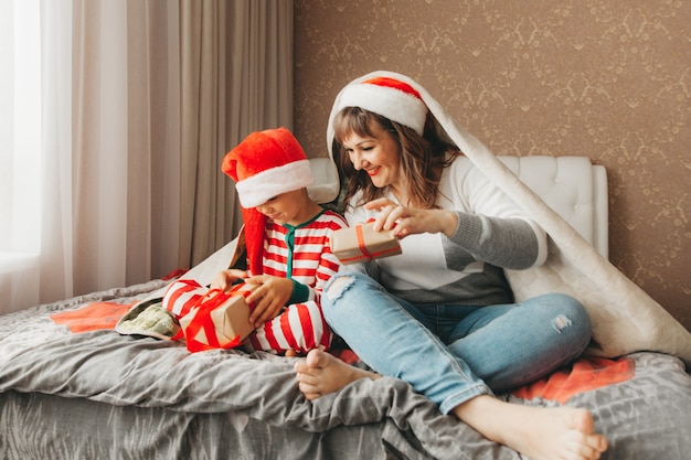 Família feliz, mãe e filho, abraçando e dando presentes na cama na manhã de Natal. Natal.