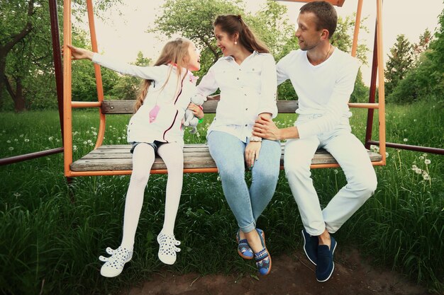 Família feliz, mãe grávida, pai feliz e filha no balanço do jardim no domingo