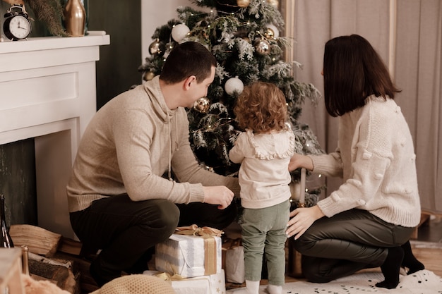 Família feliz, mãe, pai e filha perto de árvore de Natal e lareira em casa.