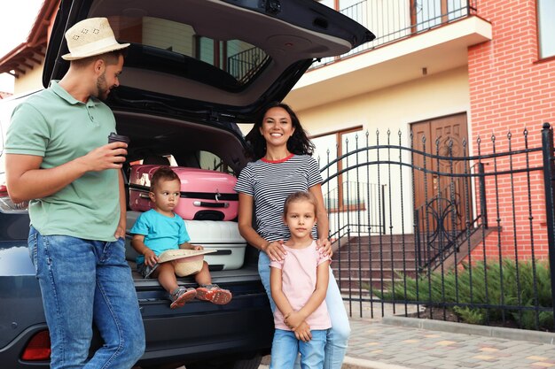 Familia feliz con maletas cerca del coche en la calle de la ciudad