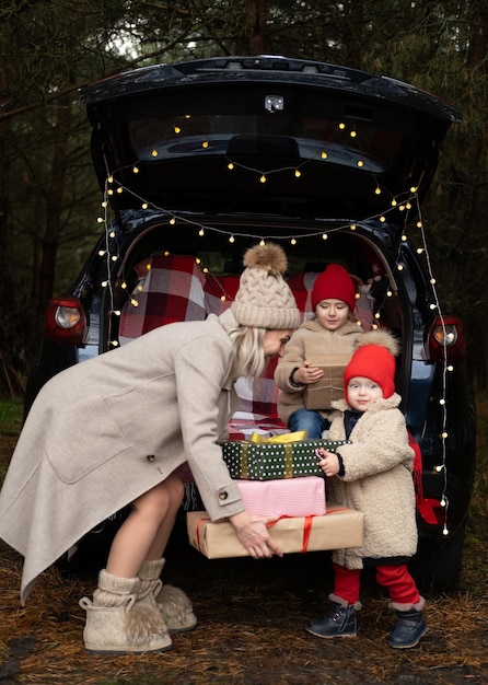 Familia feliz de mamá y dos niños con cajas de regalo de Navidad sentados en un auto decorado con Navidad