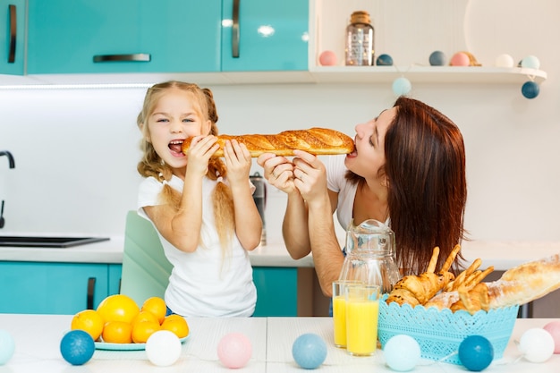 Familia feliz, mamá e hija comen un pan mordiendo desde diferentes lados. Relaciones familiares del niño con los padres.