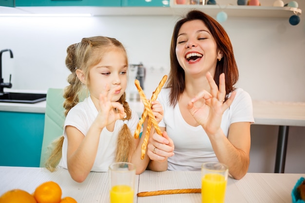 Familia feliz, mamá e hija están sentadas en la cocina y comiendo palitos de pan. Relaciones familiares del niño con los padres.