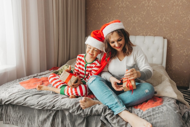 Familia feliz, mamá e hijo, abrazándose y dando regalos en la cama en la mañana de Navidad. Navidad.