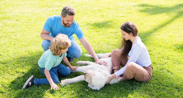 Familia feliz de mamá padre e hijo jugando con perro mascota en el parque de verano hierba verde que admite mascotas