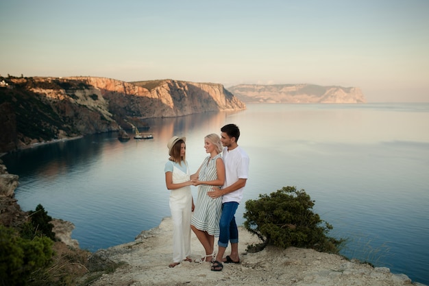 Familia feliz, mamá, papá e hija en el borde de la tierra, con vistas al mar.