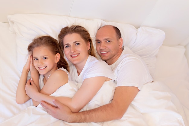 Familia feliz, mamá, papá, hija duermen en la cama en la habitación de su casa