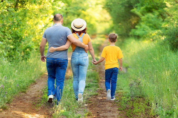 Familia feliz, mamá, papá, hijo a pie, tomados de la mano al aire libre en verano. Vista trasera