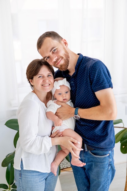 Foto familia feliz mamá papá y su pequeña hija abrazan y besan a una familia joven en casa con un bebé recién nacido