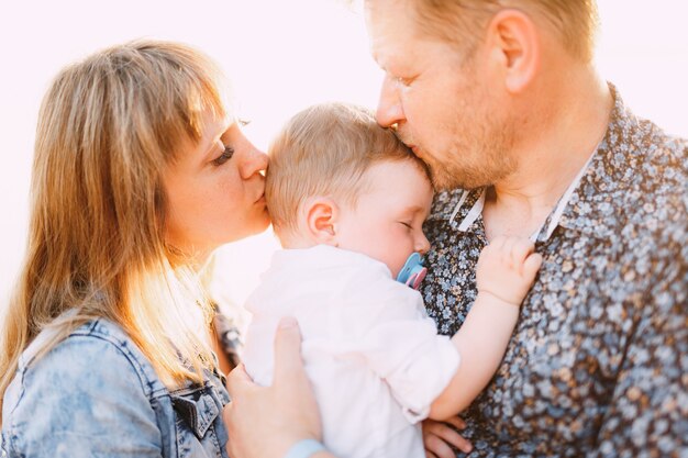 Família feliz - mamãe e papai estão segurando um filho pequeno nos braços e se beijando à beira-mar perto do