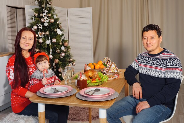 Familia feliz en la mesa en el fondo de un árbol de Navidad decorado