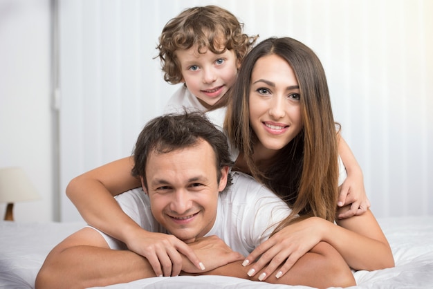 Familia feliz mirando a la cámara en su cama.