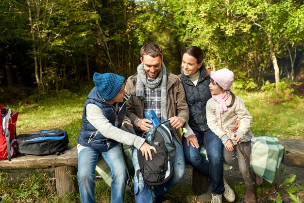 Foto familia feliz con mochilas y termos en el campamento