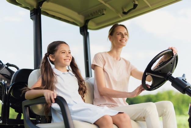 Família feliz, montando pela mãe e filha de carro de golfe.