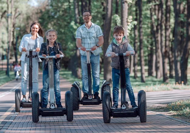 Familia feliz montando scooters eléctricos en el parque