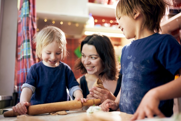 Familia feliz muchachos divertidos y su madre están preparando la masa