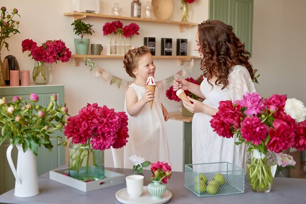 Familia feliz, mujer embarazada con pequeña hija en la cocina con flores de peonías. Relación entre padres e hijos. Maternidad, embarazo, concepto de felicidad.