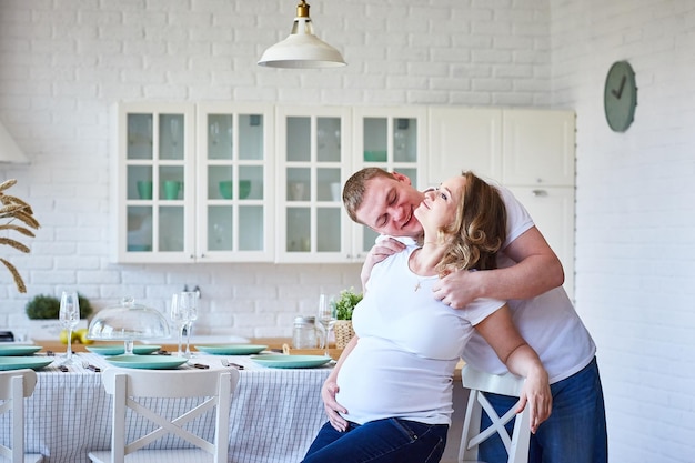 Familia feliz con mujer embarazada sentada en la cocina escandinava y divirtiéndose. Copie el espacio.