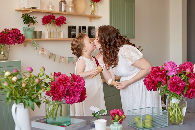 Família feliz, mulher grávida com filha na cozinha com flores de peônias. relação entre pais e filhos. maternidade, gravidez, conceito de felicidade.