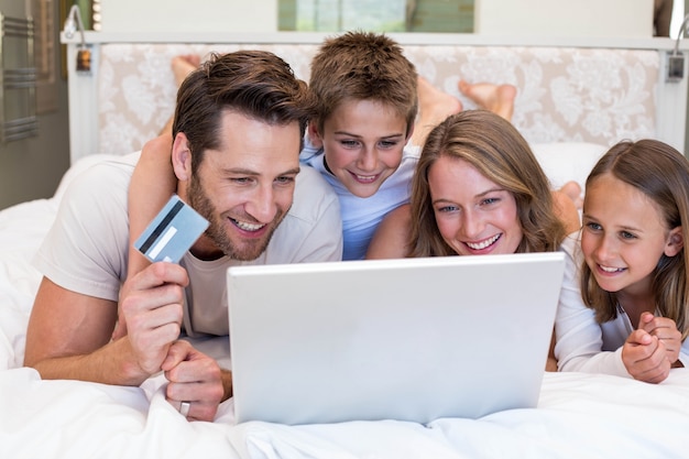 Família feliz na cama usando laptop