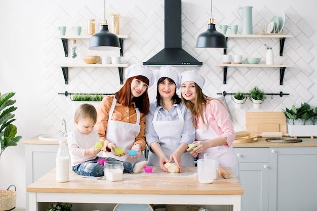 Família feliz na cozinha. Jovem e sua irmã, mulher de meia idade e filha bonita cozinhar cupcakes para o dia das mães, série de fotos de estilo de vida casual no interior da vida real