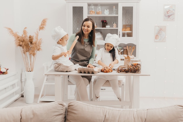 Família feliz na cozinha. mãe e filhos em trajes de cozinheiro na cozinha. mãe e filhos preparam massa, assam biscoitos