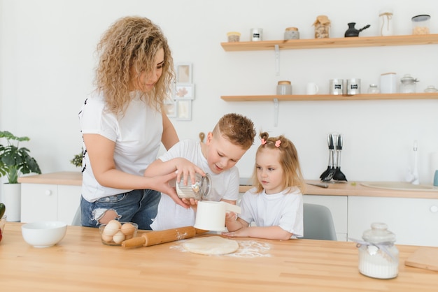 Família feliz na cozinha. mãe e filhos preparando a massa, assar biscoitos