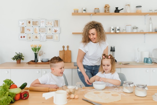 Família feliz na cozinha. mãe e filhos preparando a massa, assar biscoitos