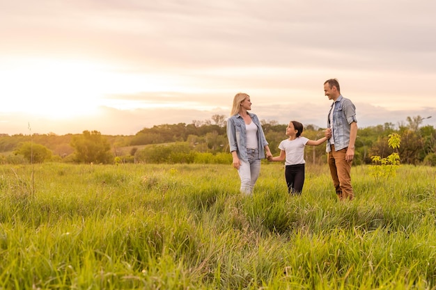 Família feliz na luz da noite do parque. As luzes de um sol. Mãe, pai e bebê caminham felizes ao pôr do sol. O conceito de uma família feliz.