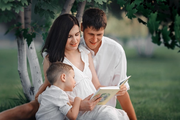 Familia feliz en la naturaleza Mamá papá e hijo leyendo un libro debajo de un árbol