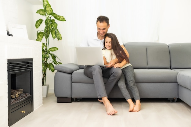 Familia feliz con niña niño divirtiéndose usando la computadora portátil juntos sentados en el sofá, los padres y la hija del niño riendo relajándose en casa con la computadora viendo videos divertidos de Internet, haciendo llamadas en línea