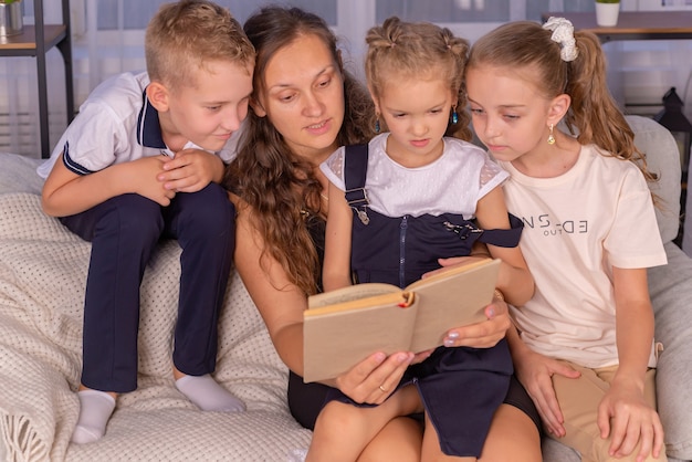 Familia feliz niñera joven mamá leyendo un libro diciéndole a los niños pequeños un divertido cuento de hadas sentado